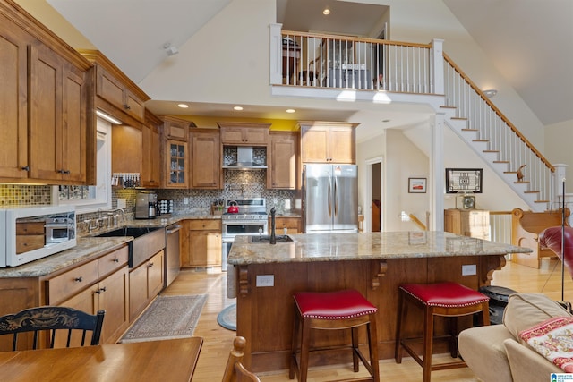 kitchen featuring light stone countertops, stainless steel appliances, light hardwood / wood-style floors, sink, and decorative backsplash