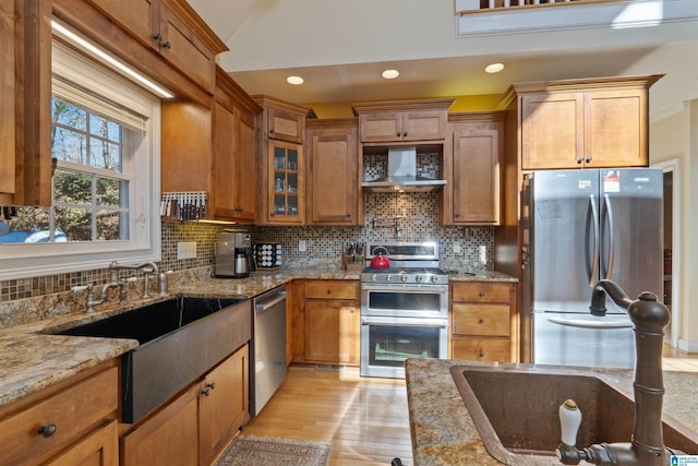 kitchen featuring appliances with stainless steel finishes, decorative backsplash, wall chimney exhaust hood, light stone counters, and sink