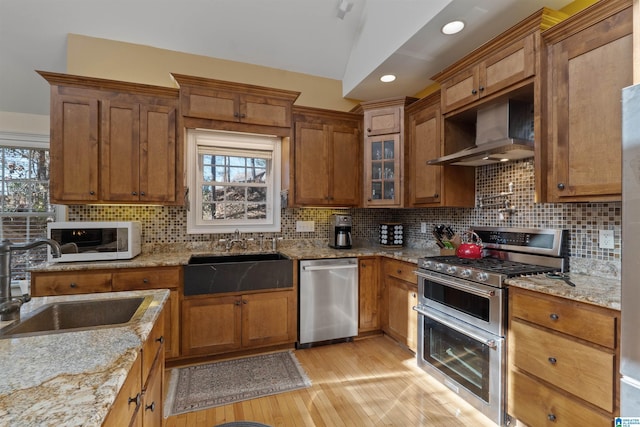 kitchen featuring light stone countertops, wall chimney exhaust hood, sink, and stainless steel appliances