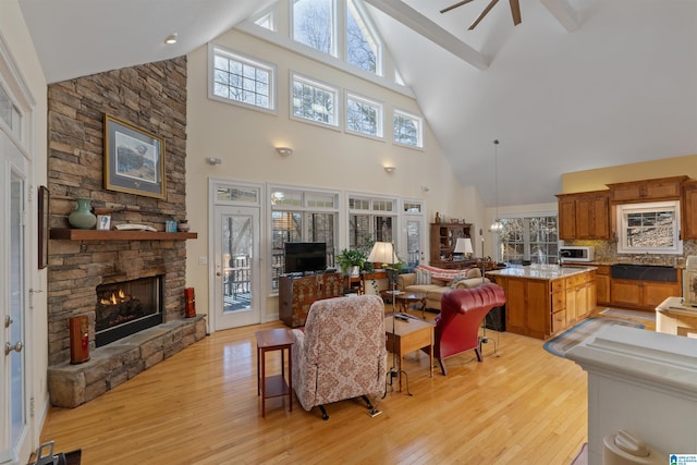 living room with high vaulted ceiling, ceiling fan, a stone fireplace, and light wood-type flooring