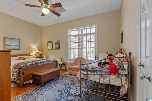 bedroom featuring ceiling fan, a drop ceiling, and hardwood / wood-style flooring