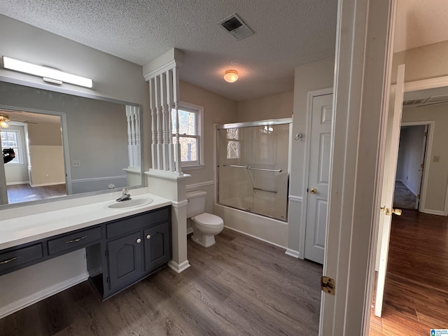 full bathroom with toilet, vanity, wood-type flooring, enclosed tub / shower combo, and a textured ceiling