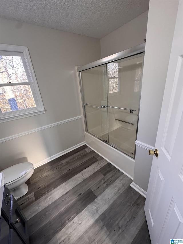 bathroom featuring a textured ceiling, toilet, wood-type flooring, and bath / shower combo with glass door