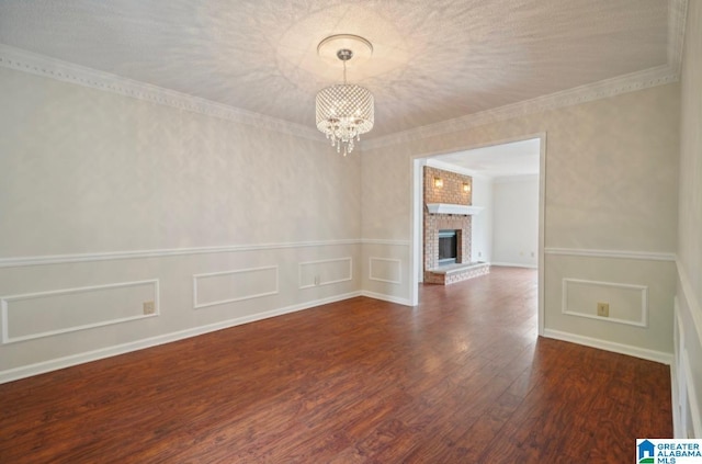 empty room featuring a fireplace, a notable chandelier, crown molding, and dark wood-type flooring