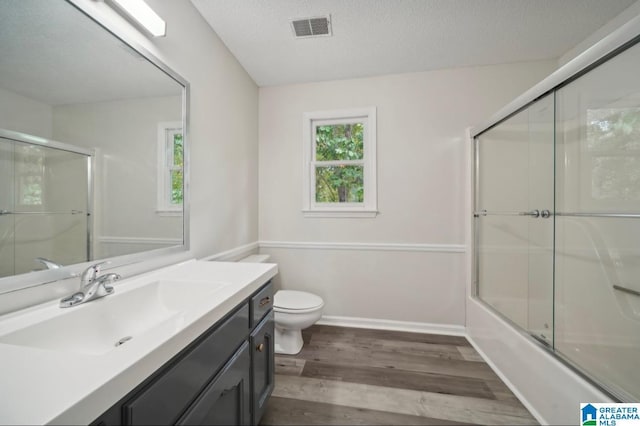 full bathroom with toilet, vanity, wood-type flooring, enclosed tub / shower combo, and a textured ceiling