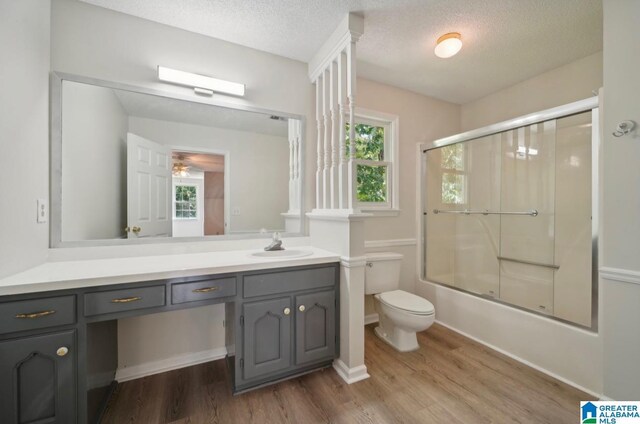 full bathroom featuring toilet, vanity, hardwood / wood-style floors, a textured ceiling, and shower / bath combination with glass door