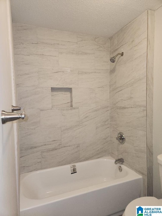 bathroom featuring a textured ceiling, toilet, and tiled shower / bath