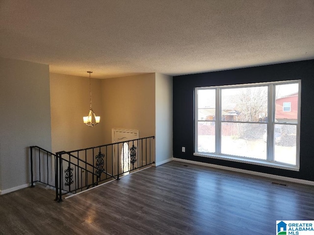 spare room featuring an inviting chandelier, dark hardwood / wood-style flooring, and a textured ceiling