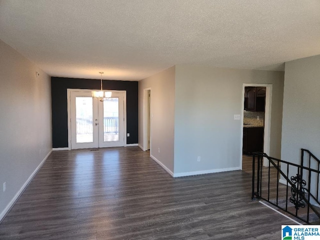 unfurnished room featuring an inviting chandelier, a textured ceiling, dark hardwood / wood-style floors, and french doors