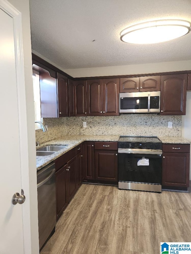 kitchen with sink, light wood-type flooring, light stone counters, a textured ceiling, and stainless steel appliances