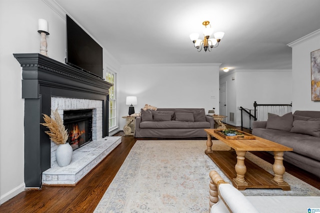 living room featuring a brick fireplace, dark hardwood / wood-style floors, ornamental molding, and an inviting chandelier