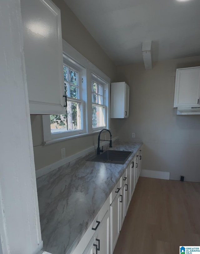 kitchen with light stone countertops, sink, white cabinetry, and light hardwood / wood-style flooring