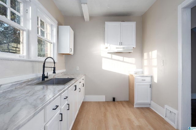 kitchen featuring white cabinetry, sink, light wood-type flooring, light stone counters, and beamed ceiling