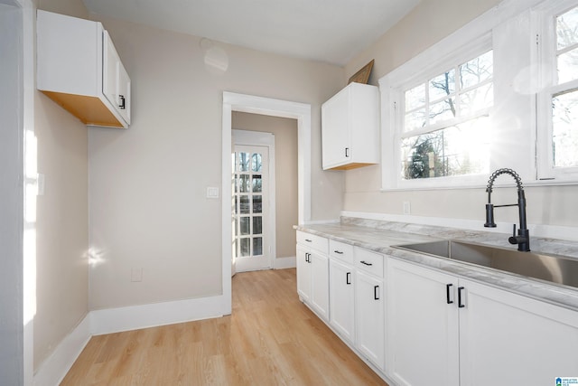 kitchen featuring light hardwood / wood-style floors, sink, light stone counters, and white cabinets