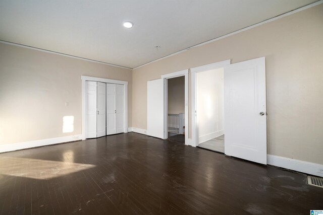 unfurnished bedroom with a closet, dark hardwood / wood-style floors, and crown molding