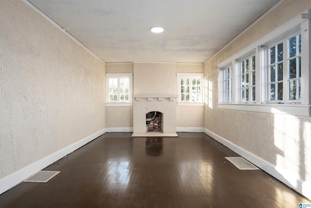 unfurnished living room with dark wood-type flooring, a brick fireplace, and a wealth of natural light