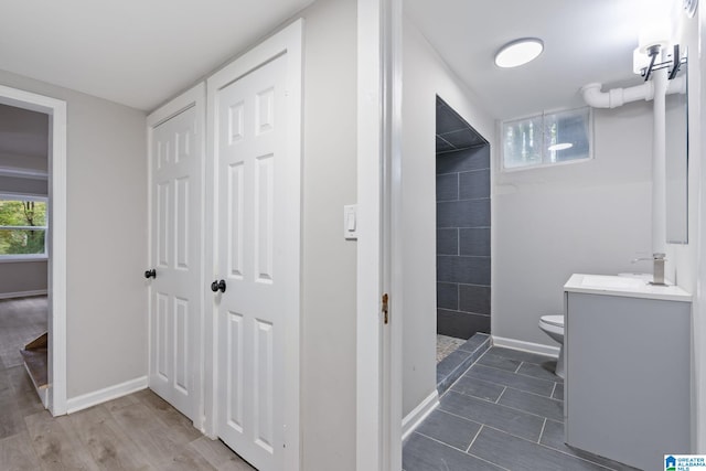 bathroom featuring toilet, vanity, wood-type flooring, and tiled shower