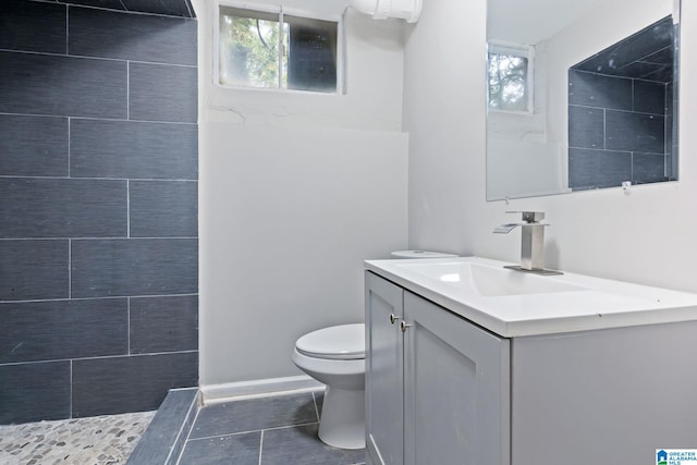 bathroom featuring toilet, a healthy amount of sunlight, vanity, and a tile shower