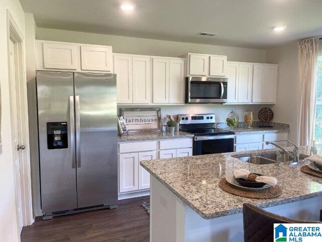 kitchen with white cabinets, appliances with stainless steel finishes, sink, dark hardwood / wood-style floors, and light stone counters