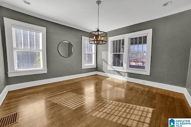 unfurnished dining area with an inviting chandelier, ornamental molding, and hardwood / wood-style floors