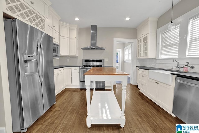 kitchen with stainless steel appliances, decorative light fixtures, dark hardwood / wood-style flooring, wall chimney exhaust hood, and white cabinets