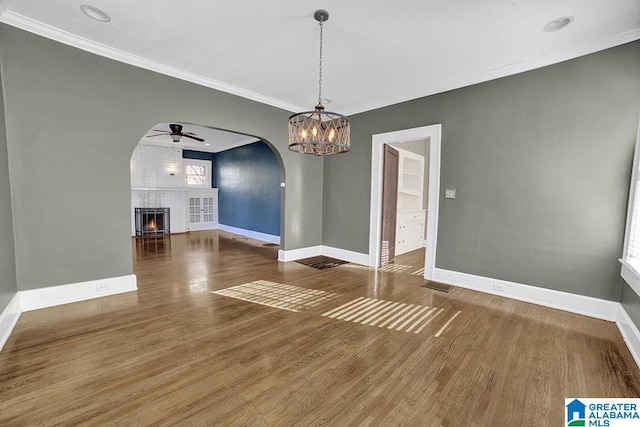 unfurnished dining area with crown molding, a brick fireplace, ceiling fan with notable chandelier, and dark hardwood / wood-style floors