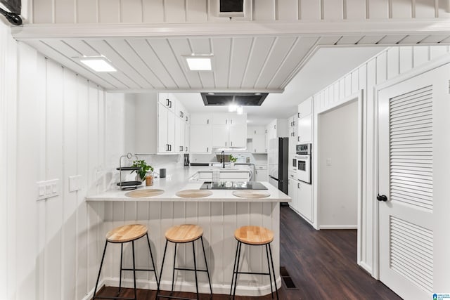 kitchen with refrigerator, white cabinetry, a kitchen breakfast bar, kitchen peninsula, and white oven