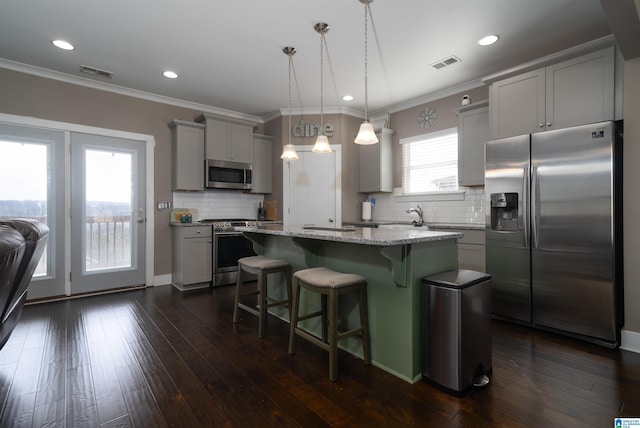 kitchen featuring a kitchen breakfast bar, a kitchen island, decorative light fixtures, stainless steel appliances, and light stone counters