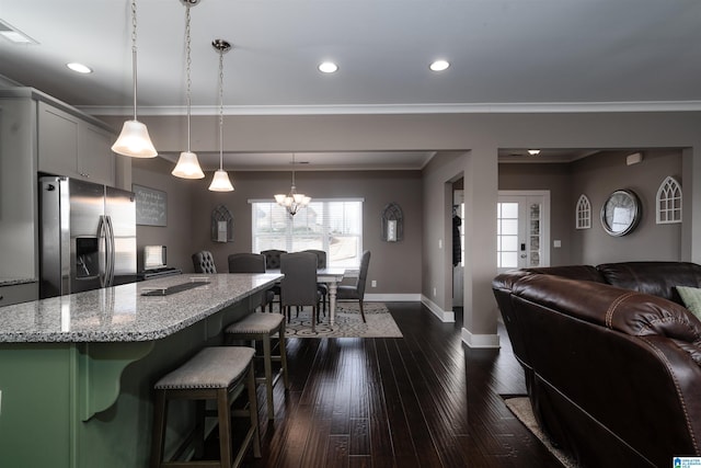 kitchen with a kitchen breakfast bar, pendant lighting, stainless steel fridge with ice dispenser, light stone counters, and an island with sink