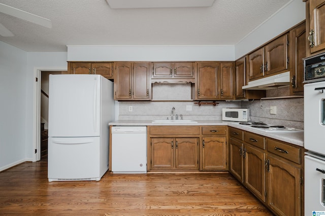 kitchen featuring white appliances, light hardwood / wood-style floors, a textured ceiling, decorative backsplash, and sink