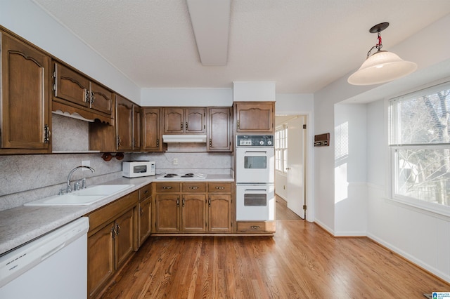 kitchen with sink, white appliances, light hardwood / wood-style flooring, and pendant lighting