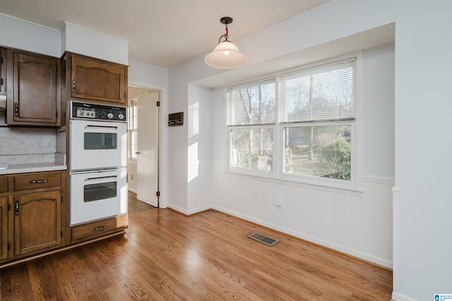 kitchen featuring pendant lighting, double oven, tasteful backsplash, hardwood / wood-style floors, and dark brown cabinetry