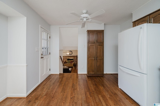 kitchen featuring a textured ceiling, a brick fireplace, white fridge, dark hardwood / wood-style flooring, and ceiling fan