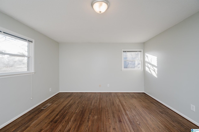 spare room featuring a healthy amount of sunlight and dark hardwood / wood-style flooring