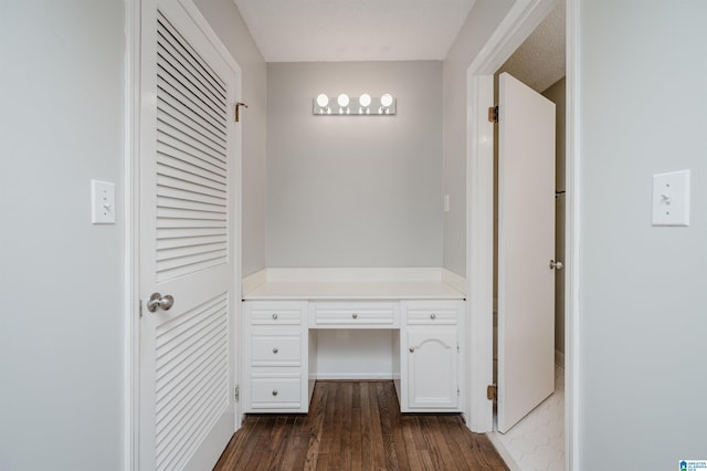 interior space with a textured ceiling, dark hardwood / wood-style floors, and built in desk