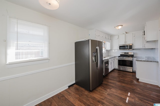 kitchen with dark wood-type flooring, light stone counters, appliances with stainless steel finishes, decorative backsplash, and white cabinets