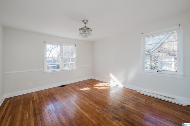 spare room with baseboard heating, a notable chandelier, wood-type flooring, and plenty of natural light