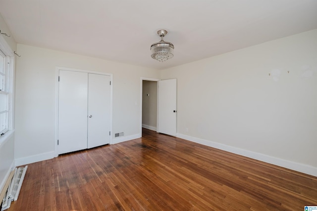 unfurnished bedroom with dark hardwood / wood-style floors, baseboard heating, and a closet