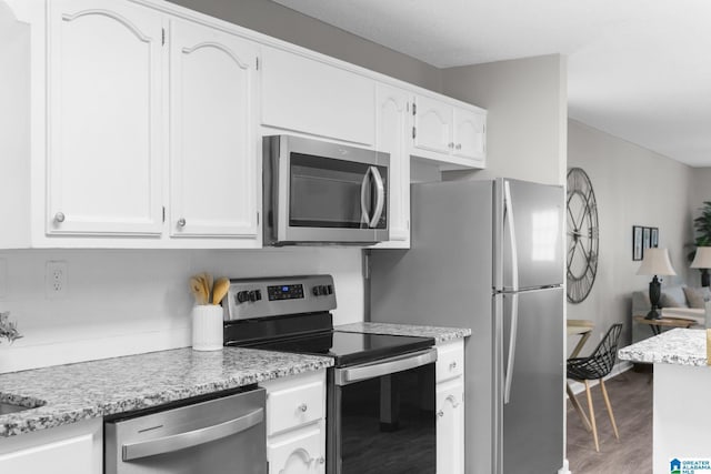 kitchen with light stone counters, hardwood / wood-style flooring, white cabinetry, and appliances with stainless steel finishes