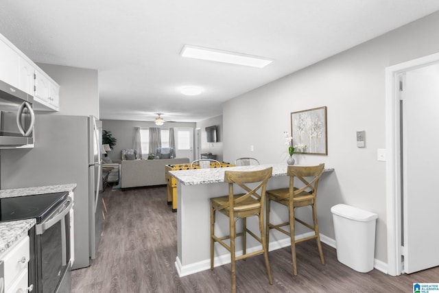 kitchen featuring appliances with stainless steel finishes, a kitchen breakfast bar, white cabinets, light stone counters, and dark hardwood / wood-style floors