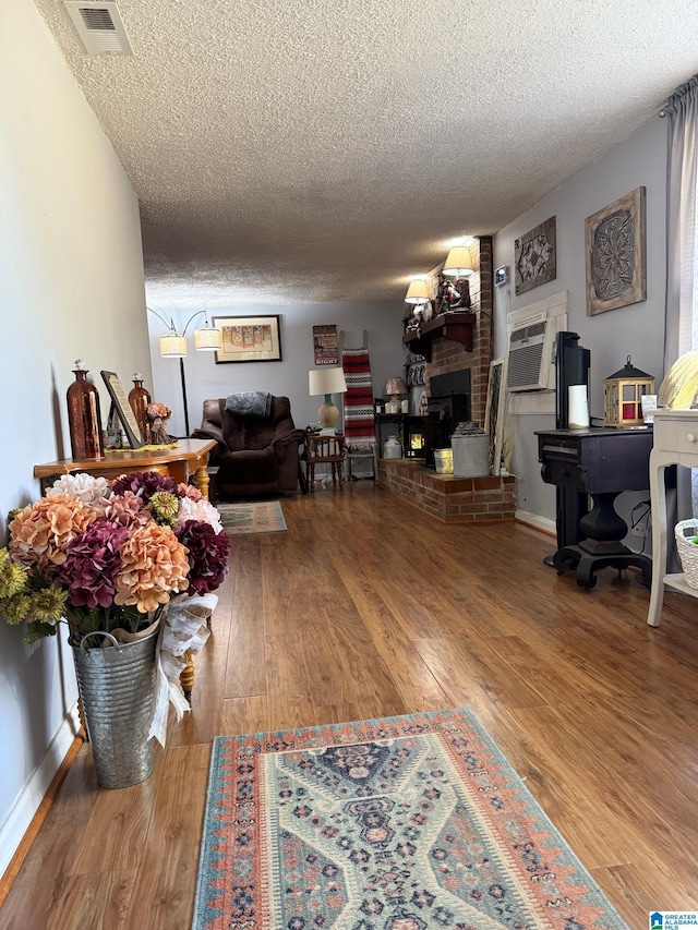 living area with a fireplace, visible vents, a textured ceiling, wood finished floors, and baseboards