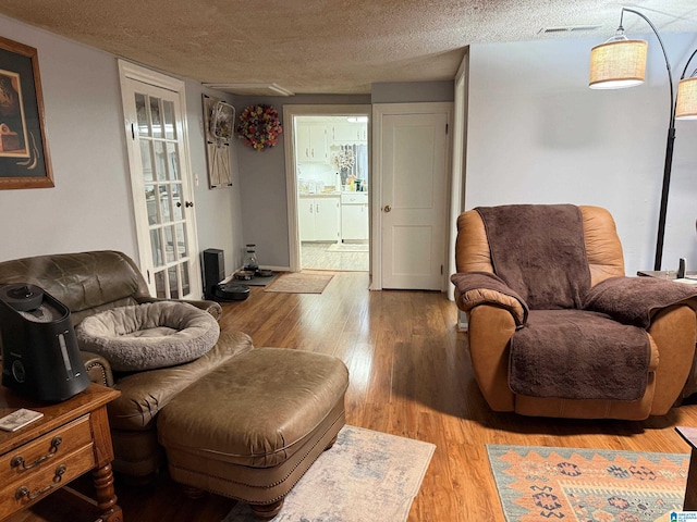 sitting room with a textured ceiling, visible vents, and wood finished floors