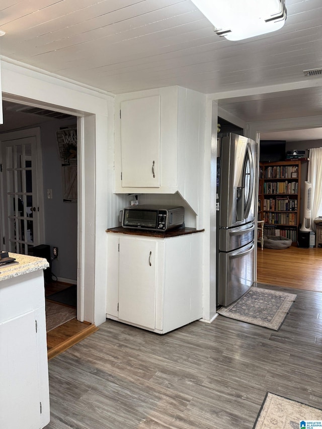 kitchen featuring stainless steel refrigerator with ice dispenser, dark wood finished floors, visible vents, and white cabinets