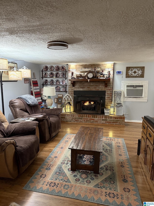 living room with a textured ceiling, a wall mounted AC, a fireplace, and light wood-style flooring