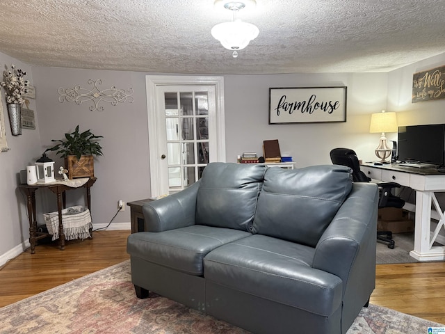 living area featuring a textured ceiling, baseboards, and wood finished floors