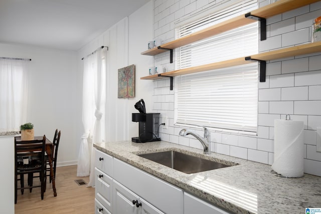 kitchen featuring light hardwood / wood-style flooring, sink, white cabinets, tasteful backsplash, and light stone counters