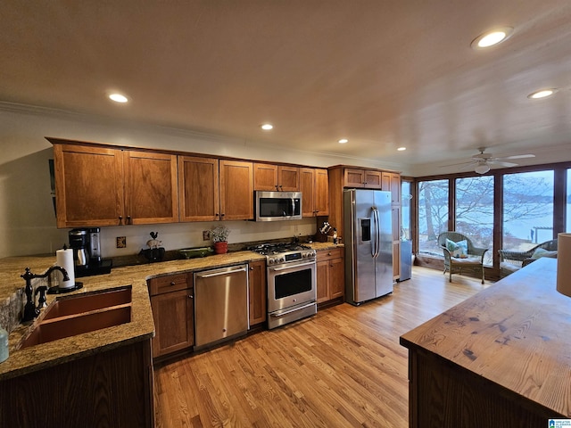 kitchen with sink, ornamental molding, light stone counters, stainless steel appliances, and light wood-type flooring