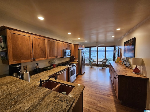 kitchen featuring sink, ornamental molding, appliances with stainless steel finishes, light stone countertops, and light hardwood / wood-style floors