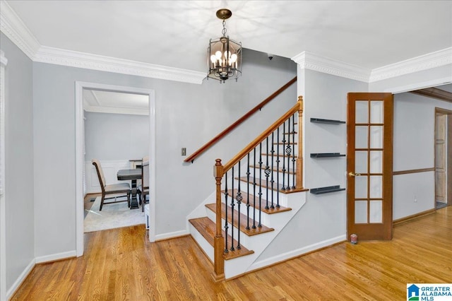 staircase with french doors, wood-type flooring, crown molding, and a notable chandelier