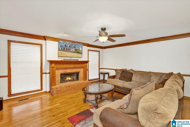 living room with ceiling fan, wood-type flooring, a brick fireplace, and ornamental molding